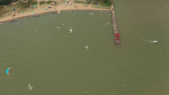 AERIAL: Reveal Shot of Bay Filled with Pro Kite Surfers Swimming in the Sea alt