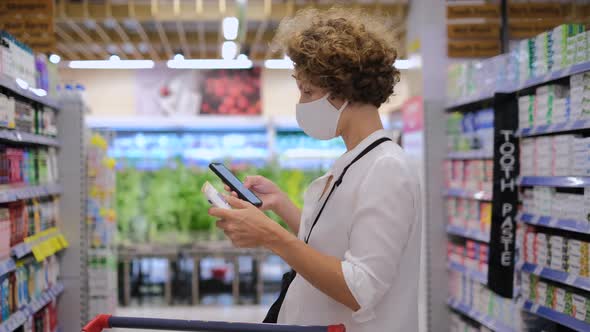 Curly Woman with Smartphone Checking the Product Surfing the Internet Between Supermarket Rows alt