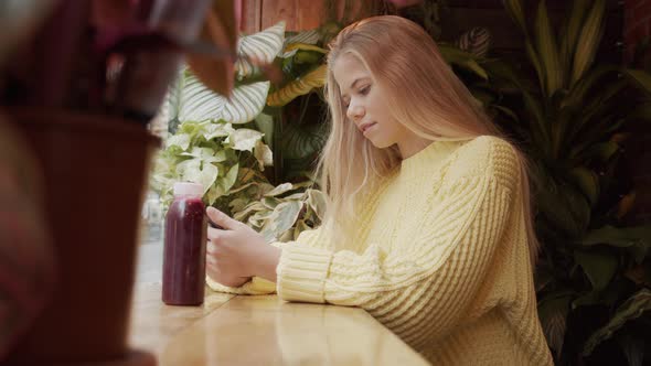 Teenage Blond Girl Looking At Phone In Cafe alt