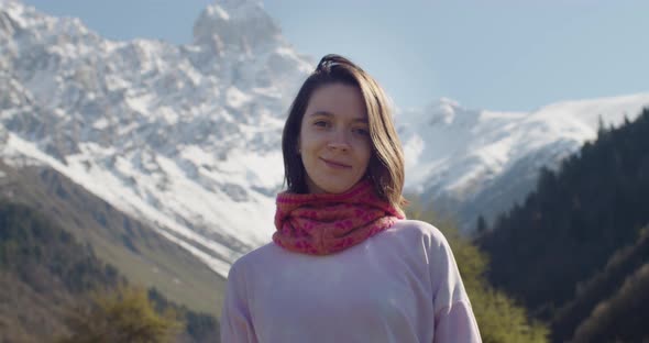 Portrait of Young Woman Looking at Camera and Smiling on Background of Snowy Mountains