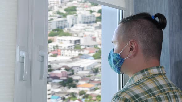 Adult Sad Man in Protective Mask Looks Out the Window During Quarantine