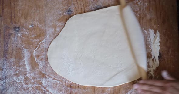 Female Hands Of Baker Rolls Dough In Flour On Wooden Board On Table With A Rolling Pin