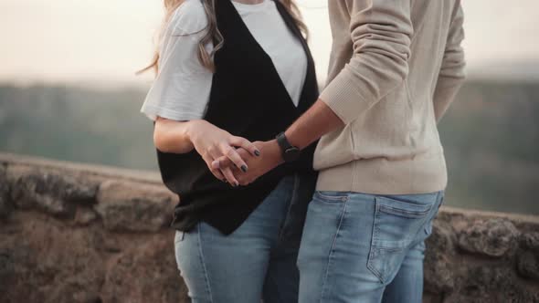 Couple Holds Hands Near The Stone Wall On A Windy Weather. medium shot alt