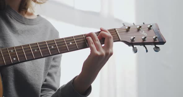 A Teenager Plays Guitar in a White Living Room with Sunlight alt