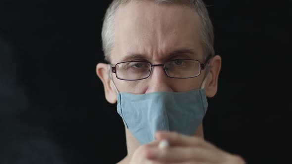 Caucasian Man Smoking a Cigarette in a Medical Mask on a Black Background