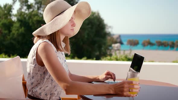 Woman in Hat Works on Laptop in Hotel Room Balcony with Sea View in Summer Day