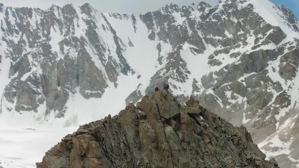 Four Climbers on Peak of Rock. Snow-Capped Mountains. Aerial View alt
