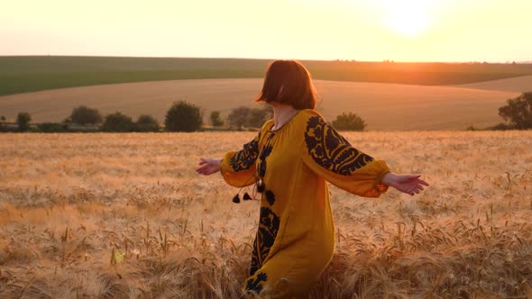 young woman in Ukrainian traditional clothes at golden field by sunset light