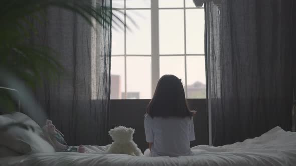 A Little Sick Girl Sits on the Bed and Hugs a Soft Toy; Drip Near