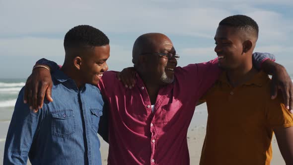 African american senior father and twin teenage sons walking on a beach and talking alt