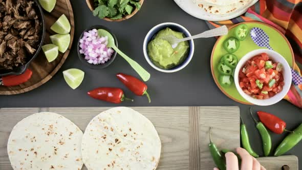 Preparing pulled pork carnitas with pico de gallo on a flour tortilla. alt
