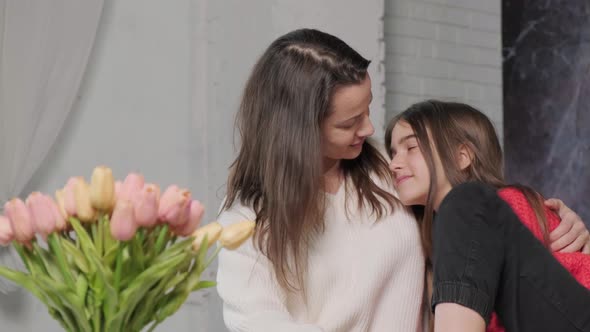 Mother Hug and Kiss Her Daughter While They are Sitting on Sofa and Talking alt