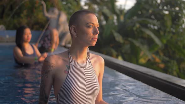 Female model contemplatively looks toward the sun in a tropical resort pool alt
