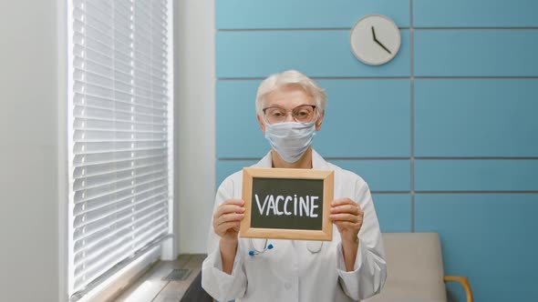 Grey haired lady doctor with protective mask holds blackboard with word Vaccine alt