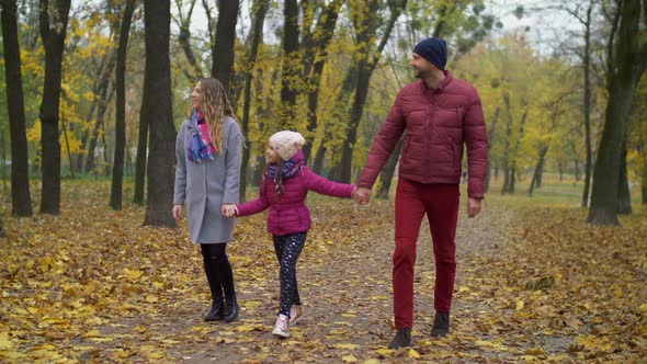 Cheerful Family with Girl Walking in Autumn Park alt