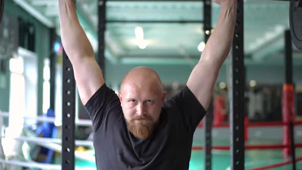 Front View Bald Sportsman with Red Beard Lifting Barbell in Slow Motion Looking at Camera alt