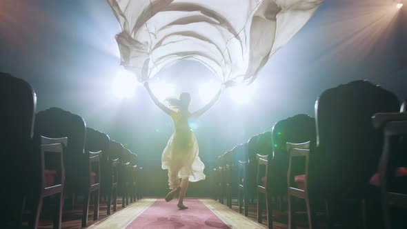A young woman runs through the theatre, the wind blows, white light fabric develops. muse of art.