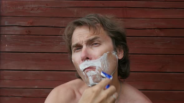 Middle Age Man Shaves His Beard With Foam, Sitting In Yard, Outside. 