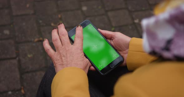 Close Up Hands Woman Holding Phone with Vertical Green Screen on Busy Street Background Pavement alt