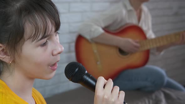 The girl sings into a microphone to live music.  alt