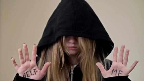 Teenage Girl Covering Her Face with a Hood Shows Her Palms with the Inscription HELP ME alt