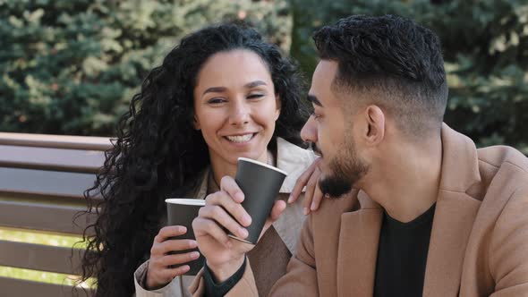 Close Up Young Hispanic Couple Sitting on Bench in Autumn City Park Man and Woman Drinking Coffee alt