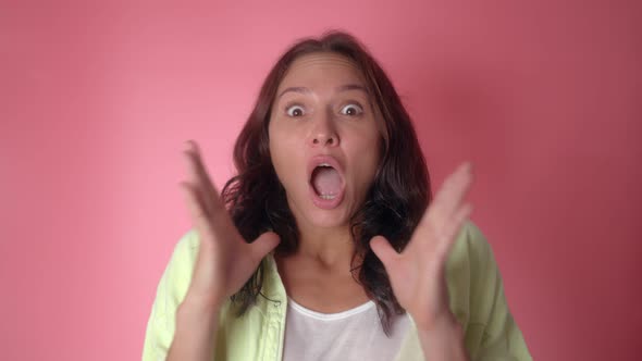 Shocked Woman Face with Opened Mouth and Eyes Looking to Camera on a Pink Wall Background alt