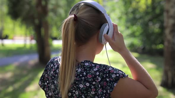 Woman Puts on Headphones in the Park ,Back View