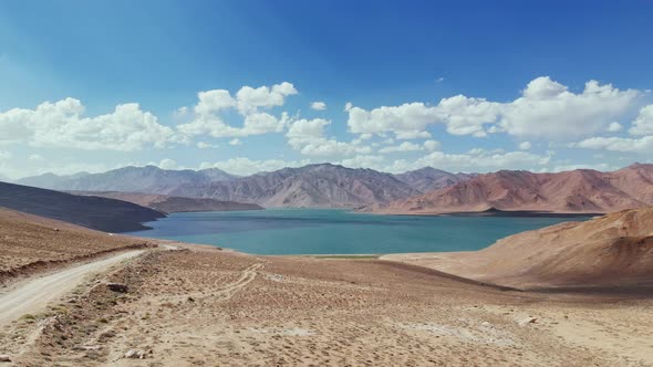 Aerial Over Gravel Road Path Toward Bulunkul Lake in Sunny Day alt