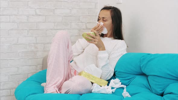Sick Young Woman Sits of Sofa and Blowing Nose in Paper Tissue at Home