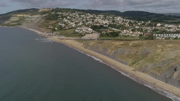Aerial tracking from sea in towards the village of Charmouth. Amazing Jurassic coast cliffs surround alt
