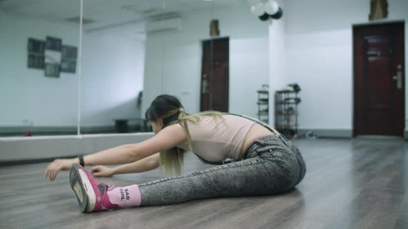 Caucasian female dancer choreographer stretching and warming up on the floor of a dance studio alt