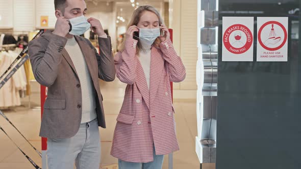 Couple Putting On Face Masks Before Entering Clothing Store alt