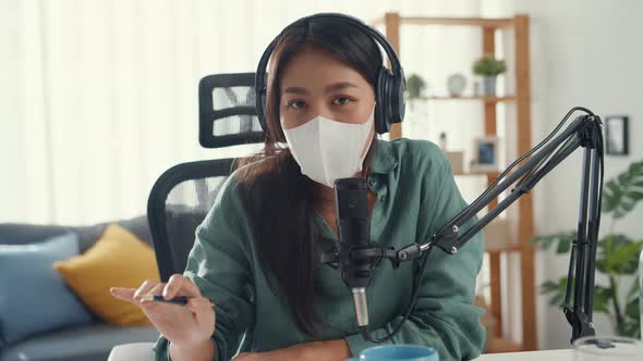 Asia girl record podcast use headphones and microphone wear mask protect virus look at camera talk.