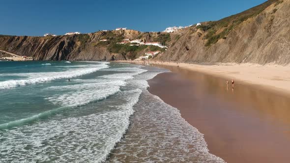 Aerial drone shot of whitewater waves rolling in on a beach next to sandy cliffs. alt