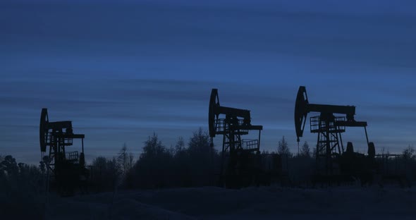 Three Dark Silhouettes of Oil Rigs on a Common Plan in a Winter Field alt