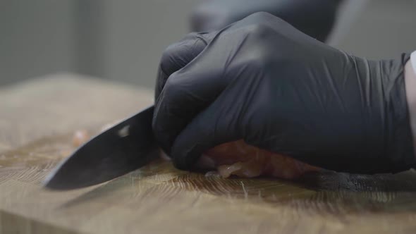 Hands of Chef in Restaurant Uniform and Black Gloves Cutting Slices of Tuna Fish alt