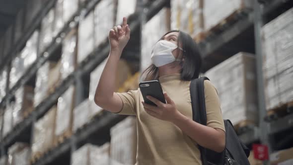 Asian woman wearing mask walking in warehouse and use smart phone.