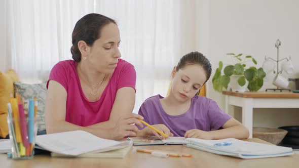 Mother helping her young daughter prepare homework during homeschooling alt