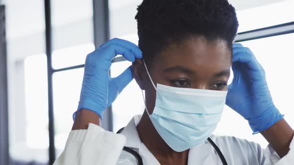 Portrait of african american female doctor wearing surgical gloves putting on face mask alt
