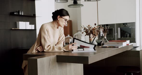 Serious Relaxed Woman Reading Book at Modern Home in Cozy Kitchen Interior alt
