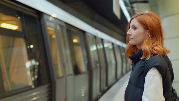 Tourist female waiting at platform of metro station looking at passing train. alt