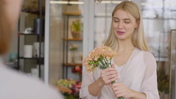 Happy Female Customer Smelling Carnations and Talking to Florist in Shop alt
