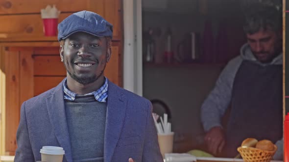 Smiling man standing with coffee near street cafe