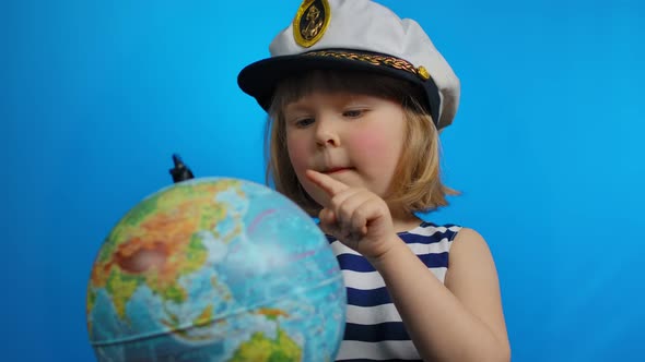 Little Blond Girl in Sailor Hat is Pointing Her Finger Into the Globe and Smiles alt