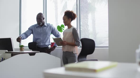 Diverse businessman and businesswoman talking, woman using digital tablet in office alt
