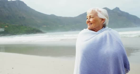 Senior woman covering herself with blanket on beach alt