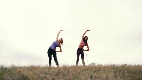 Two Young Fitness Woman Doing Exercises on the Gym in an Outdoor on the Sky Background alt