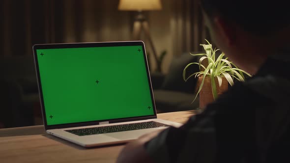 Teenage Boy Sitting At His Desk Learning Online On A Laptop With Green Mock-Up Screen At Home alt