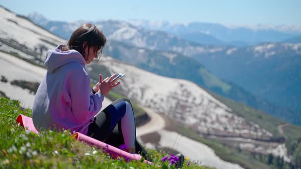 Woman with Smartphone at Top of Mount Tourist is Resting After Hiking in Mountains alt